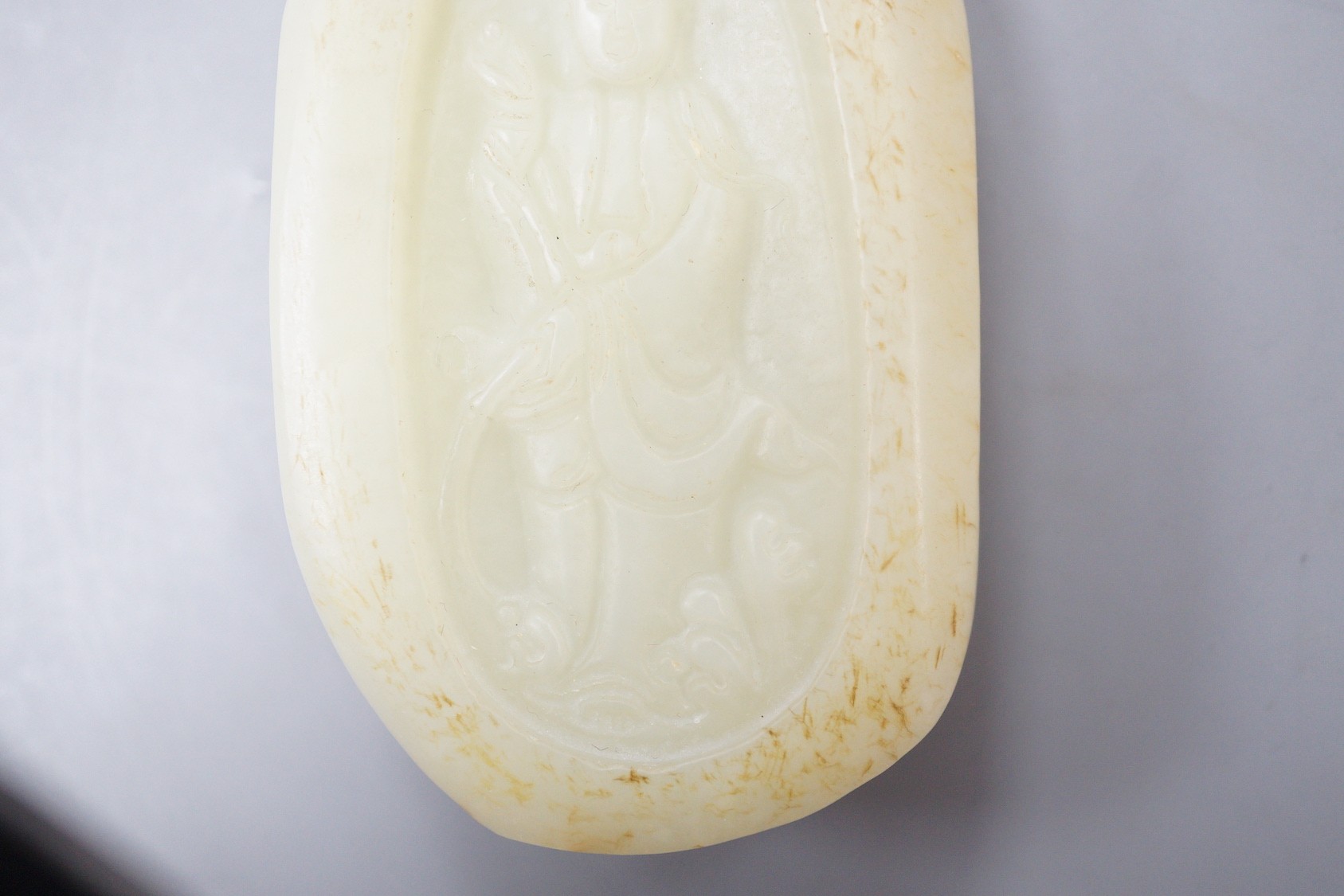 A Chinese celadon jade pebble carving depicting Guanyin, 7.5cm tall